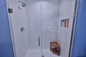Ducha envuelta en vidrio con ducha de mano y estante con artículos de aseo.