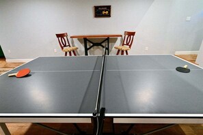 Una mesa de ping pong con dos sillas y una mesa al fondo.