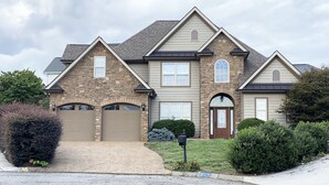 A two-story house with a stone facade, a brown garage door, and a front entrance with a brown door and a decorative window.