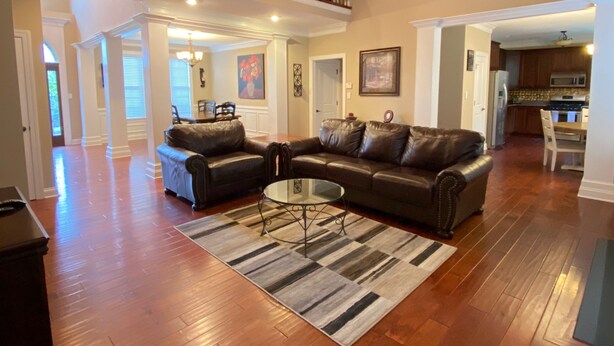 A spacious living room with hardwood floors, a leather sectional sofa, a glass coffee table, and a ceiling fan.