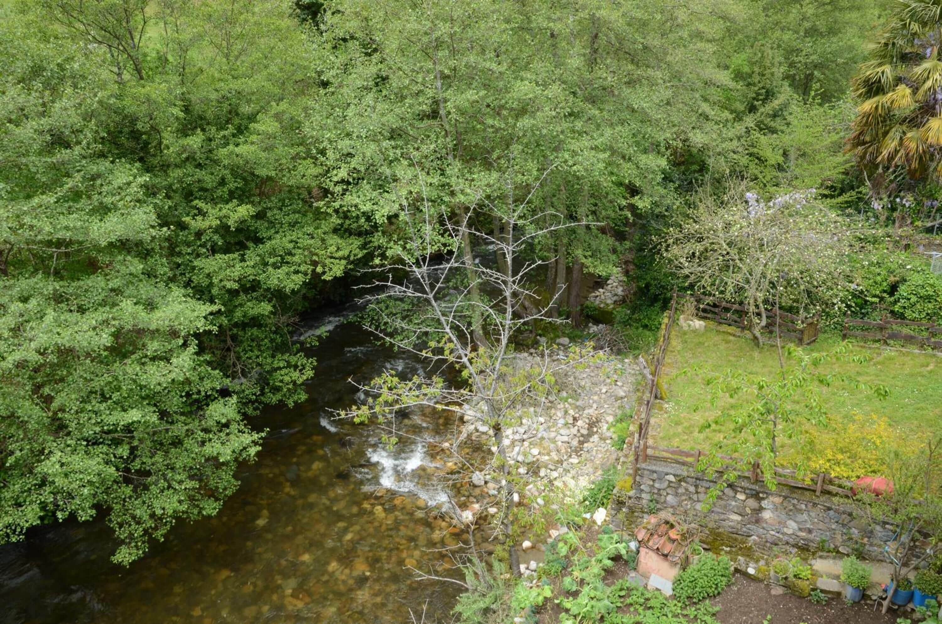 Un río serpentea por una zona boscosa con un muro de piedra y un pequeño jardín.