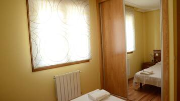 Een slaapkamer met een houten vloer, een witte radiator, een bed met een witte dekbedovertrek en een grote spiegel die de kamer weerkaatst.