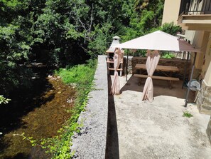 A patio area with a concrete floor, a small stream, and a wooden table and bench. - El Rincón de Limés (Cangas del Narcea)