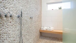 Een badkamer met een wand met een steenachtig oppervlak, een douche, een raam en een plank met opgevouwen handdoeken.