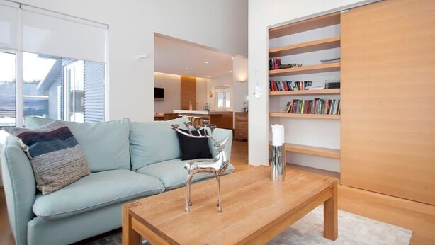 Een moderne woonkamer met een lichtblauwe bank, een houten salontafel en een boekenplank vol boeken.