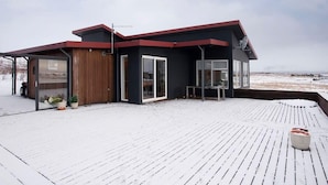 Een modern huis met een houten terras en een rood dak.