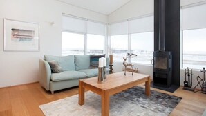 Een moderne woonkamer met een bank, een houten salontafel, een open haard en grote ramen met uitzicht op zee.