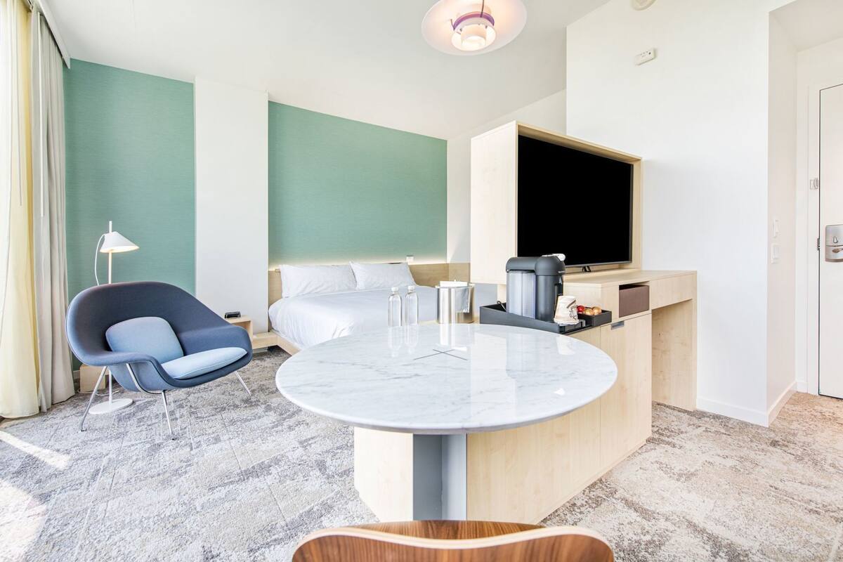 Een moderne hotelkamer met een bed, een bureau met een flatscreen-televisie, een stoel en een ronde tafel.
