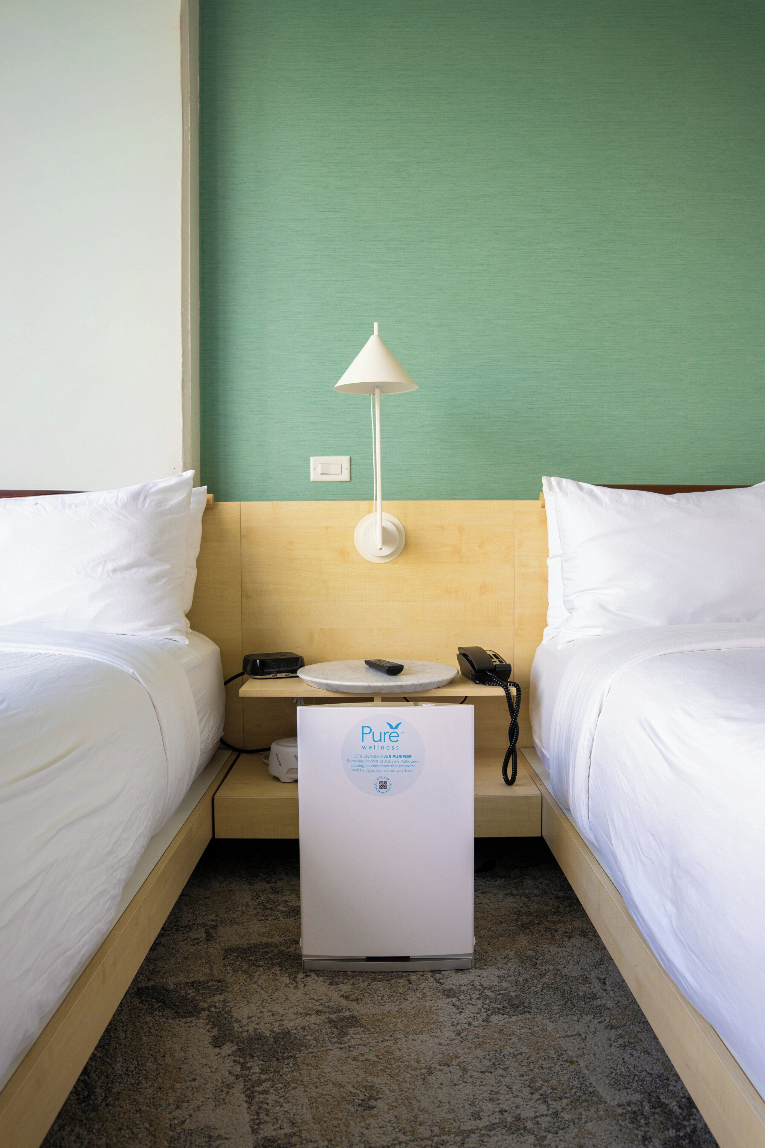 Habitación de hotel con dos camas, una mesita de noche pequeña, una lámpara, un teléfono y un purificador de aire portátil.