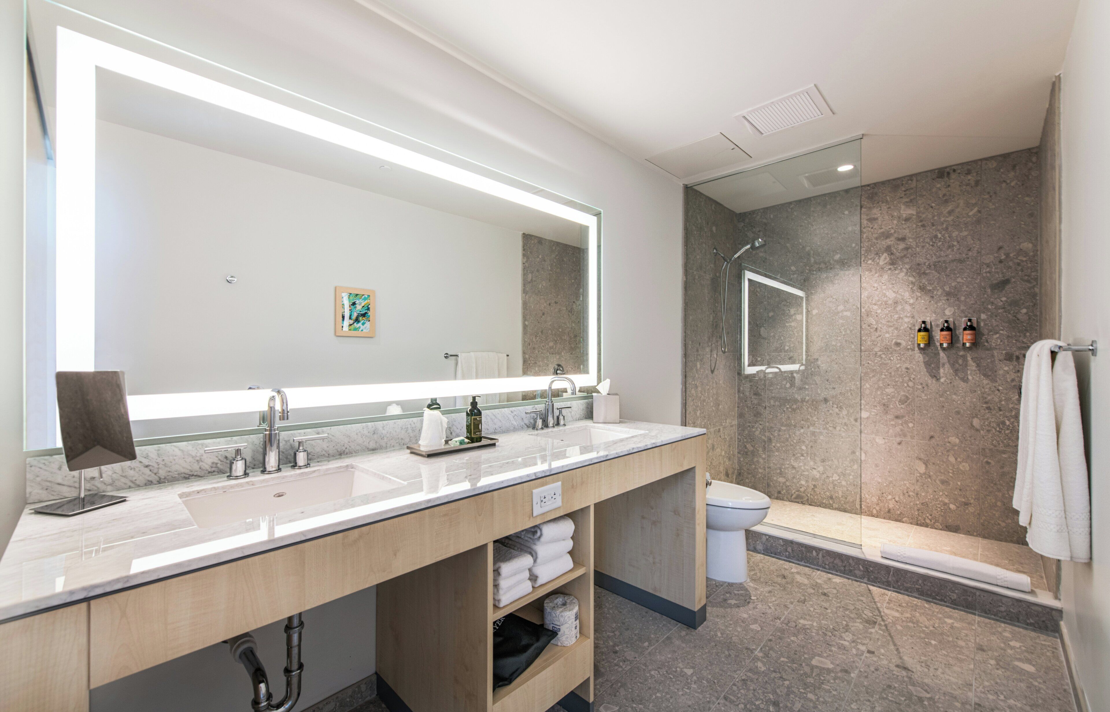 Un baño moderno con un espejo grande, dos lavamanos, ducha e inodoro.