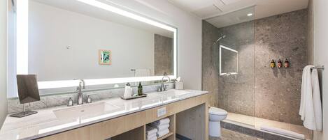 Un baño moderno con un espejo grande, dos lavamanos, ducha e inodoro.