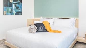 Una cama impecable con un peluche, una almohada negra con el logotipo del hotel y un plaid amarillo.