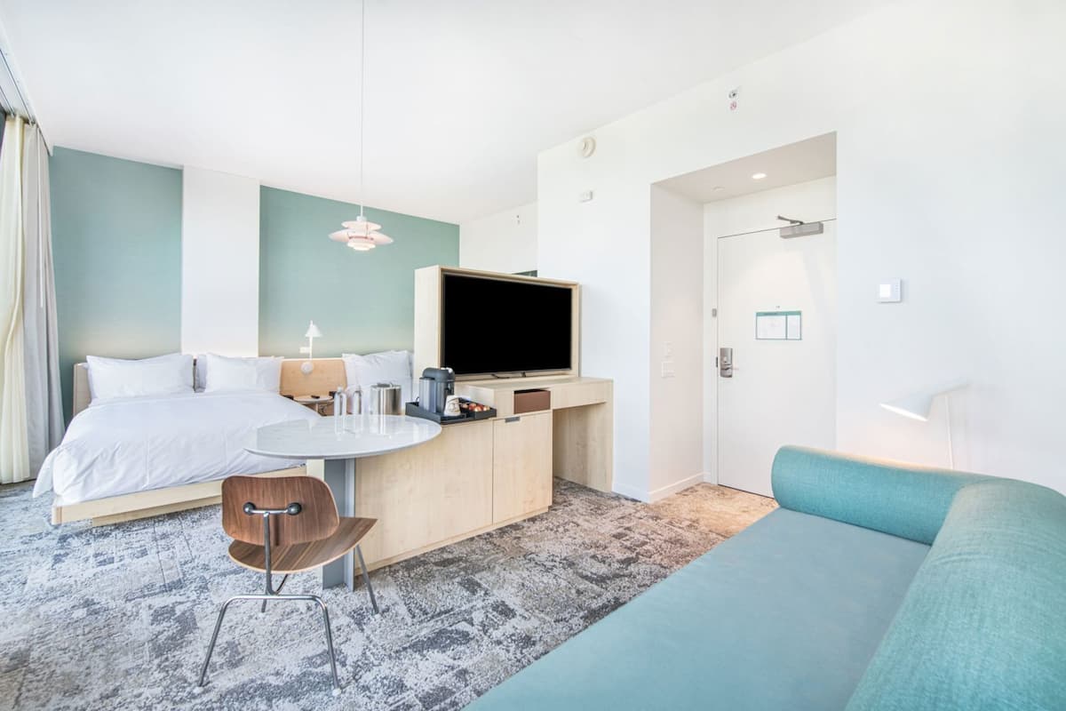 Een moderne hotelkamer met een bed, een klein bureau met een televisie, een bank en een stoel.