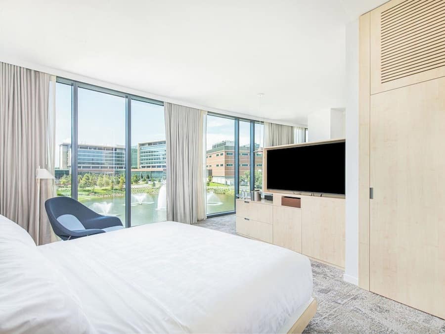 Habitación de hotel con una cama grande, televisor, una silla y vista a un edificio y una fuente de agua.