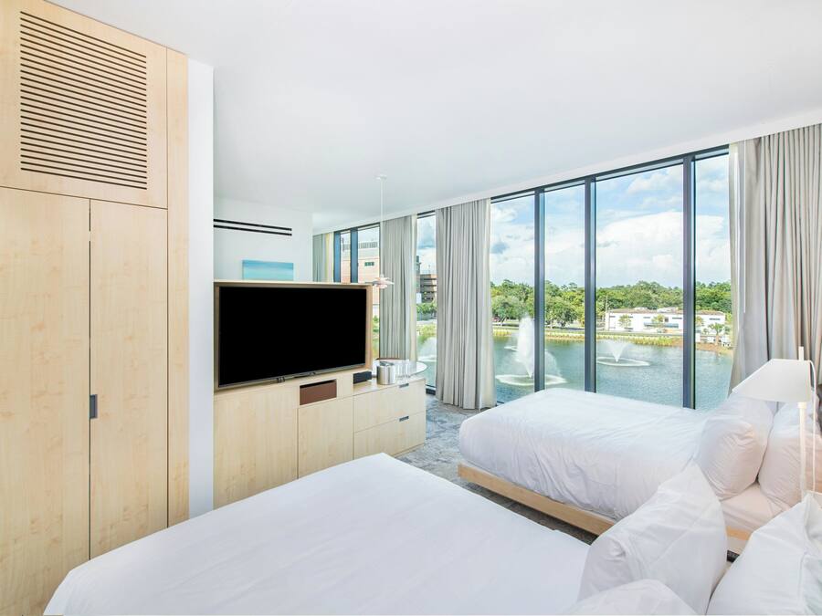 A hotel room with two beds, a television, and a large window with a view of a body of water and buildings.