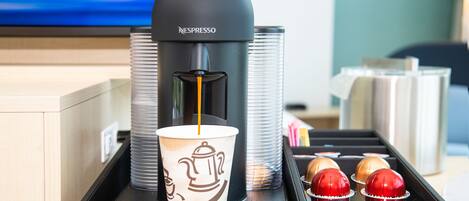 A Nespresso coffee machine dispensing coffee into a cup, with a tray containing a cup and two red and gold coffee cups.
