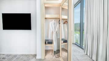 A modern hotel room with a large flat-screen TV, a walk-in closet with a mirror, and a view of a building and a fountain through the window.