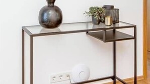 A modern console table with a glass top and metal frame, a large mirror above it, and a vase and plant on the table. - Tyr 2BR apartment (Reykjavík)
