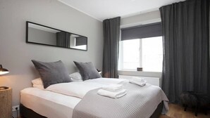 A modern hotel room with a large bed, a bedside lamp, a window with curtains, and a mirror on the wall. - Tyr 2BR apartment (Reykjavík)