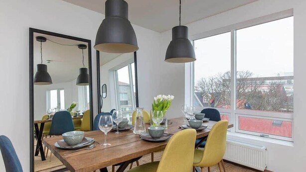 A dining area with a wooden table, yellow chairs, black pendant lights, and a large mirror on the wall. - Tyr 2BR apartment (Reykjavík)