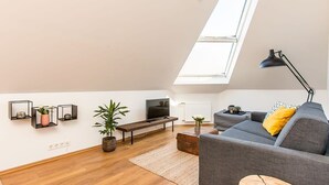 A modern living room with a loft bed, a flat-screen TV, a grey sofa, and a skylight. - Tyr 2BR apartment (Reykjavík)