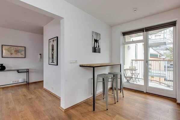 Un interior moderno con suelo de madera, una mesa de comedor con taburetes y un amplio ventanal corredero que da a un balcón exterior.
