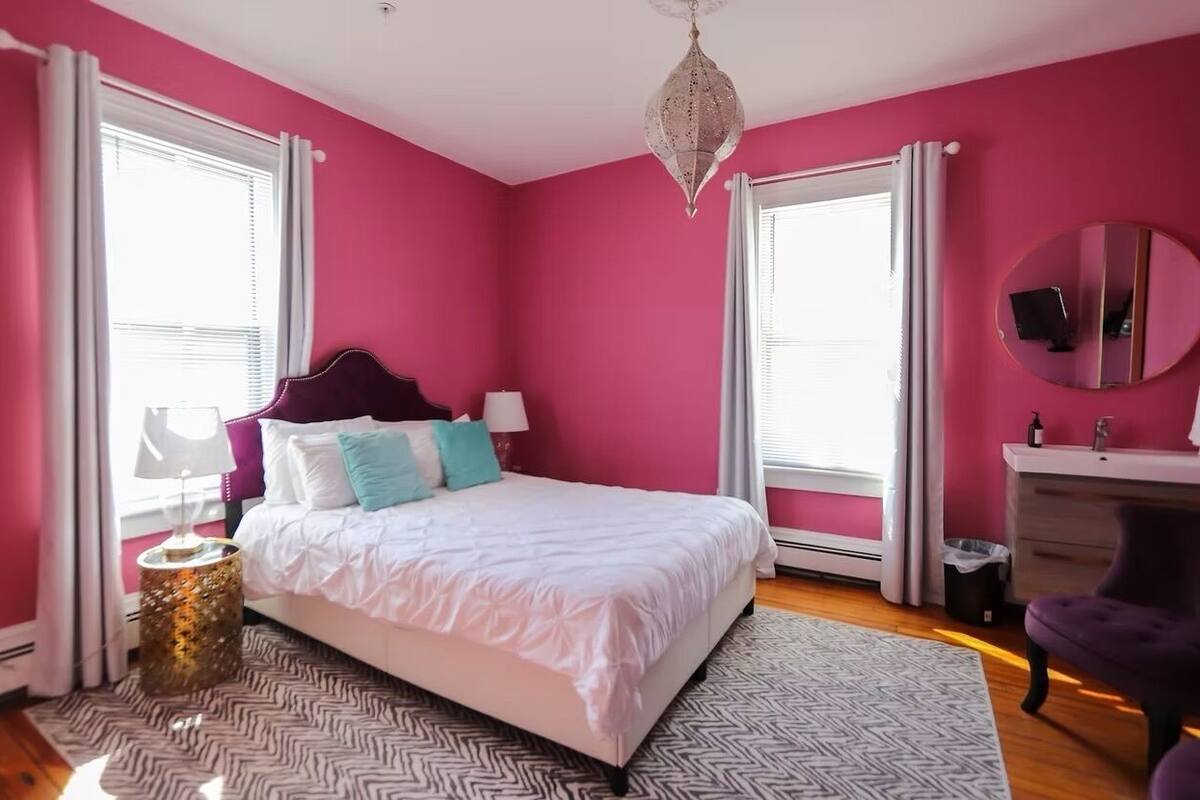 A bedroom with a bed, a bedside table, a lamp, a dresser, a mirror, and a chandelier.