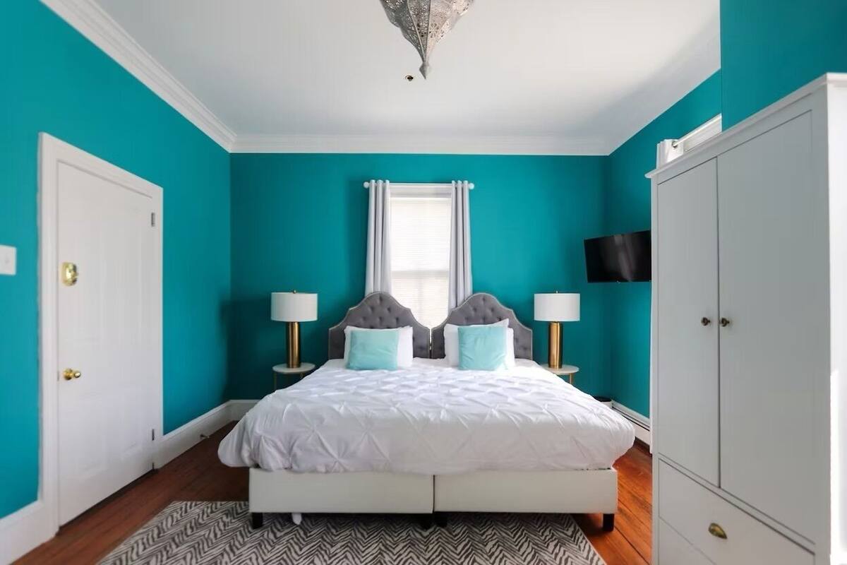 A bedroom with a bed, two bedside tables, a wardrobe, a window with curtains, and a ceiling light fixture.