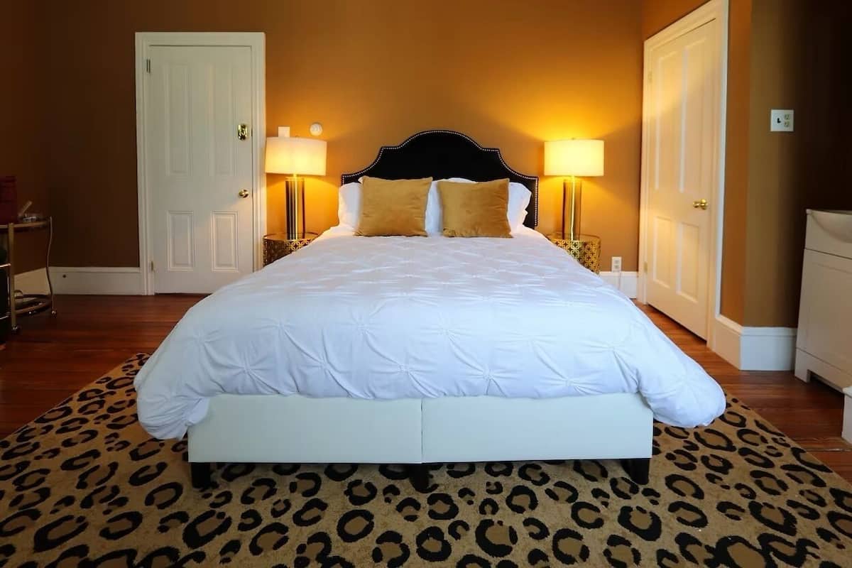 A bedroom with a large bed, two bedside lamps, a leopard print rug, and a white door.