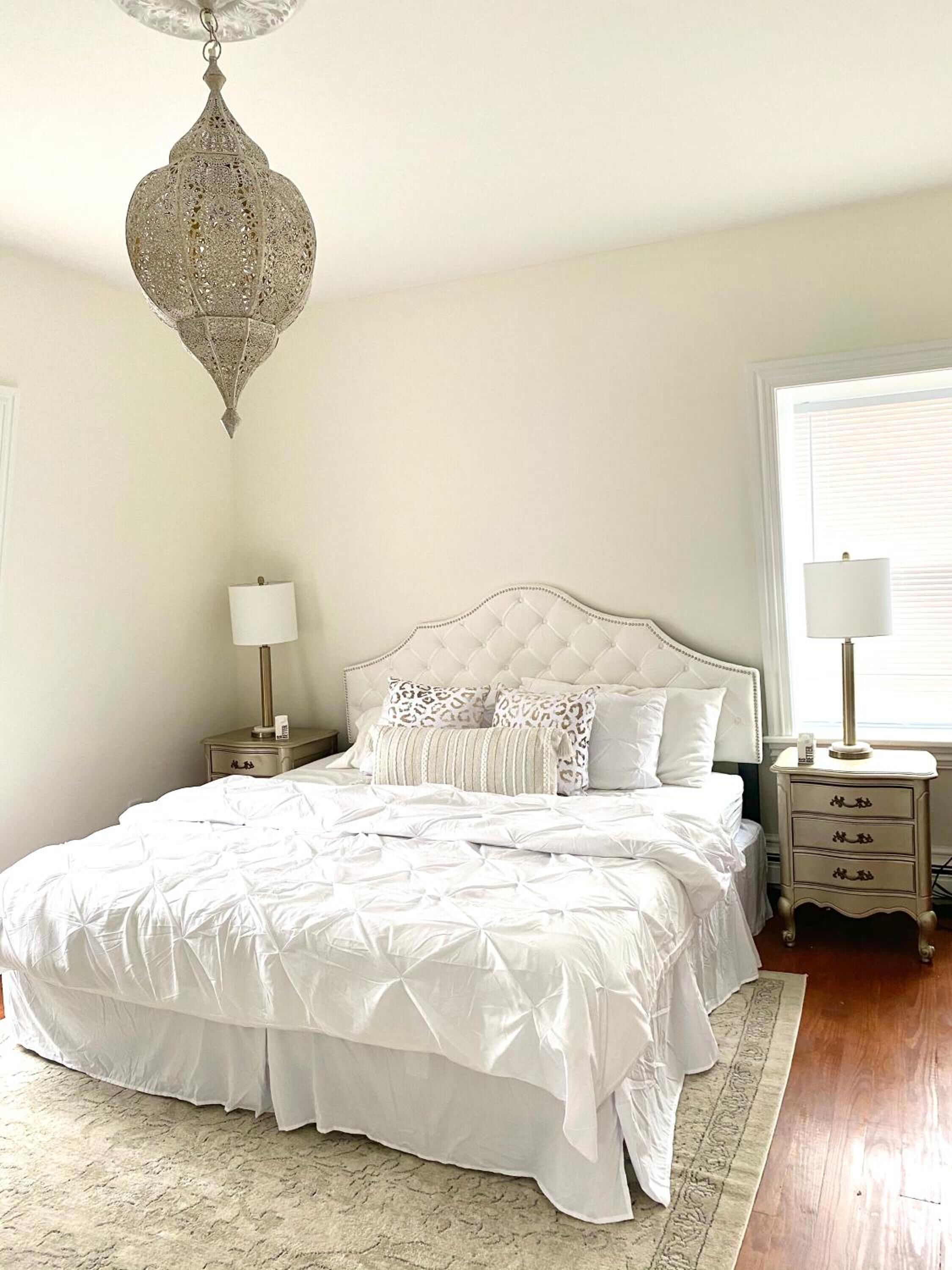 A neatly arranged bedroom with a large bed, two bedside tables, a hanging light fixture, and a window with blinds.
