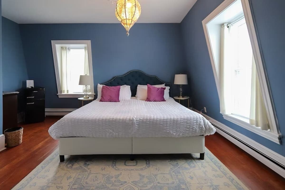 A bedroom with a bed, two bedside tables, a nightstand, a chandelier, a window, and a door.