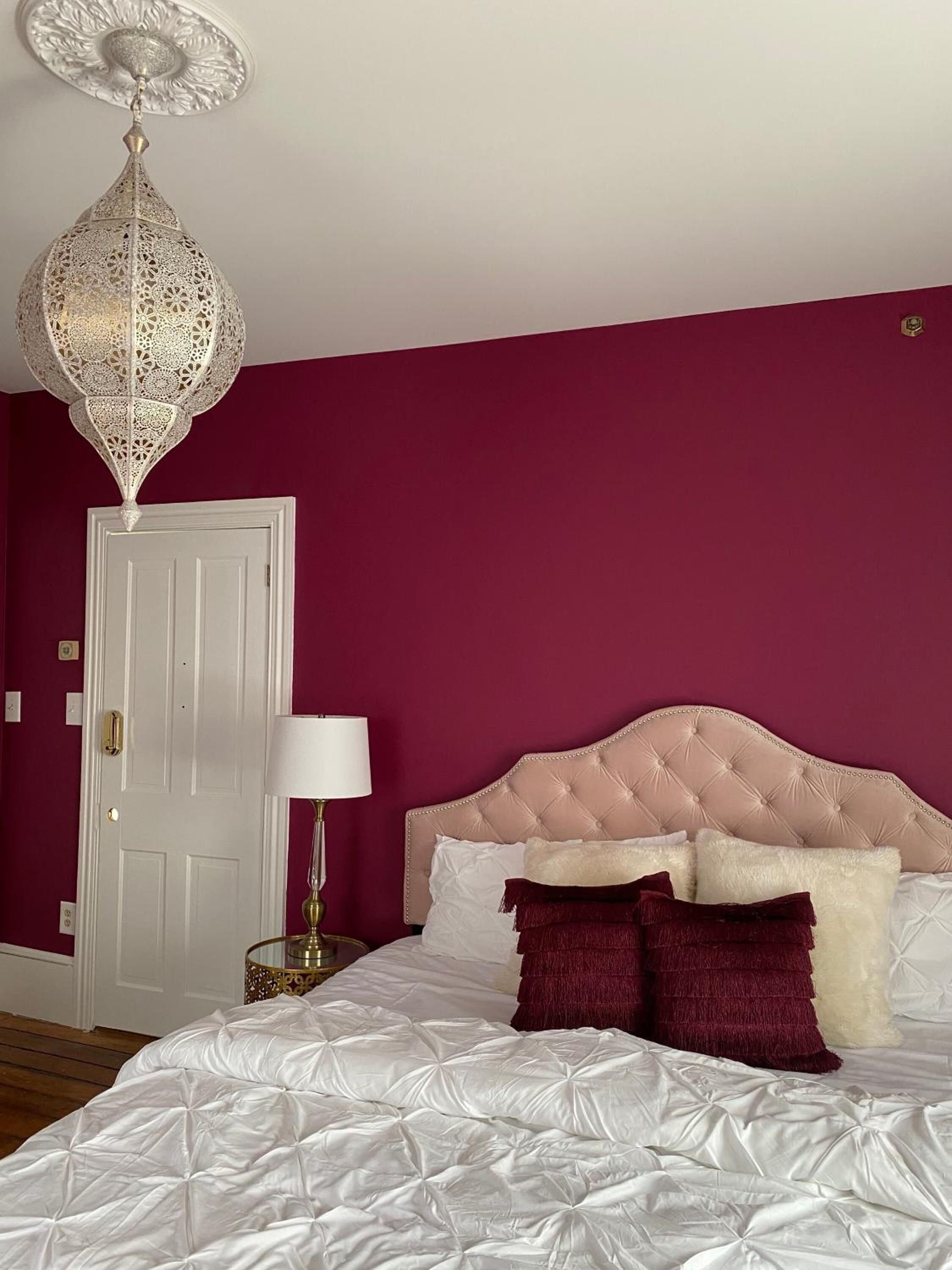 A bedroom with a tufted headboard, a white bedspread, and a decorative hanging light fixture.
