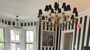 Una sala de estar con un sofá color beige, paredes a rayas negras y blancas, una araña y un piano.