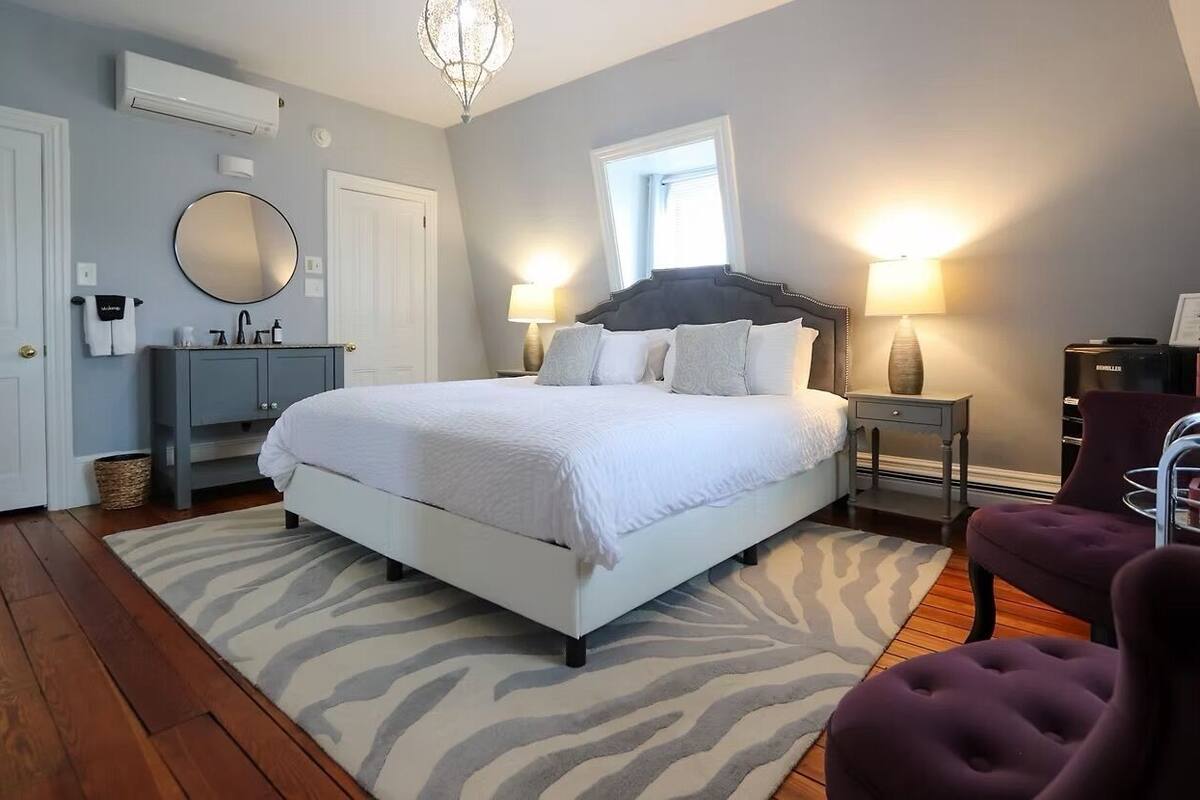 A bedroom with a bed, bedside tables, a mirror, a window, and a zebra-patterned rug.
