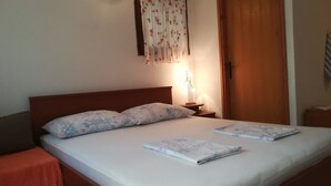 A neatly made bed with floral-patterned pillows and a folded blanket, a bedside table with a lamp, and a wooden headboard.