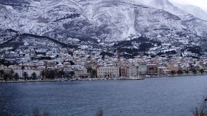 A coastal town with a marina, buildings, and snow-covered mountains in the background.