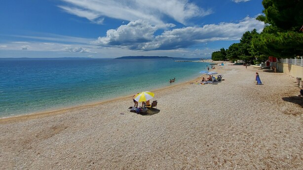 A pebbled beach with umbrellas, a clear sky, and a distant shoreline.