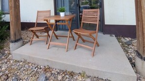 An outdoor seating area with two wooden chairs and a table, under a wooden pergola, in front of a building with a glass door and an air conditioning unit on the wall. - Modern Condo only Minutes from Deadwood & Sturgis! (Lead)