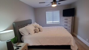 A bedroom with a bed, a nightstand, a lamp, a ceiling fan, a window with blinds, and a TV on a dresser. - Modern Condo only Minutes from Deadwood & Sturgis! (Lead)