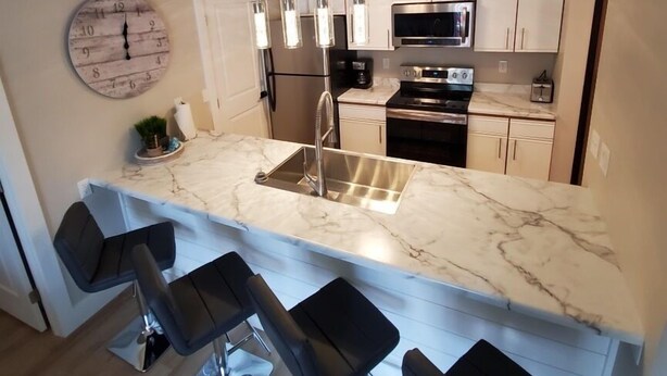 A modern kitchen with a marble countertop, stainless steel appliances, and bar stools. - Modern Condo only Minutes from Deadwood & Sturgis! (Lead)