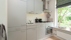 Cucina moderna con mobili bianchi, lavello in acciaio inossidabile, piano cottura a gas e una finestra vista verde.
