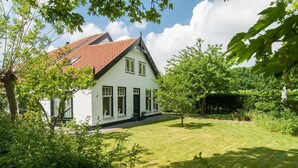 Una casa bianca con tetto rosso, circondata da vegetazione e alberi.