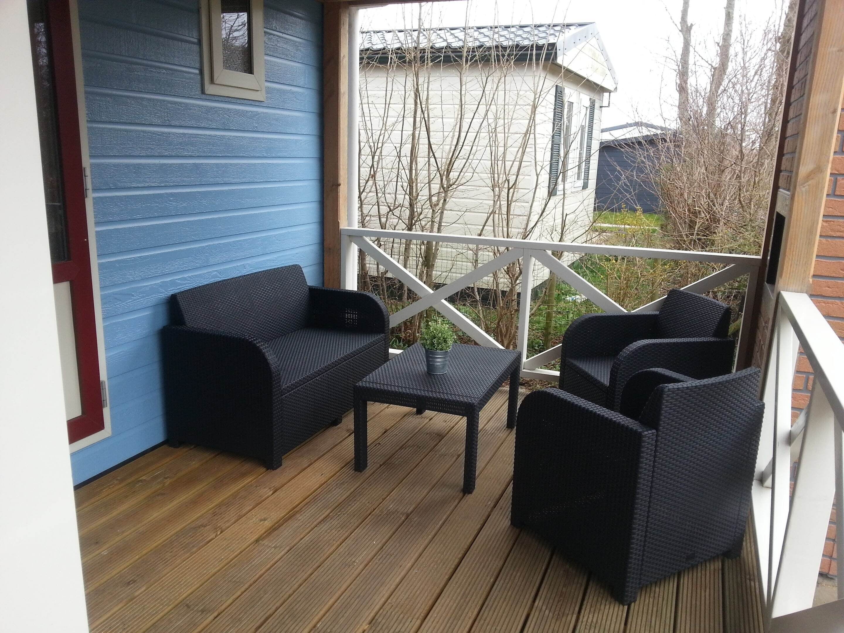 A covered outdoor seating area with a blue wall, a wooden deck, and a white railing.