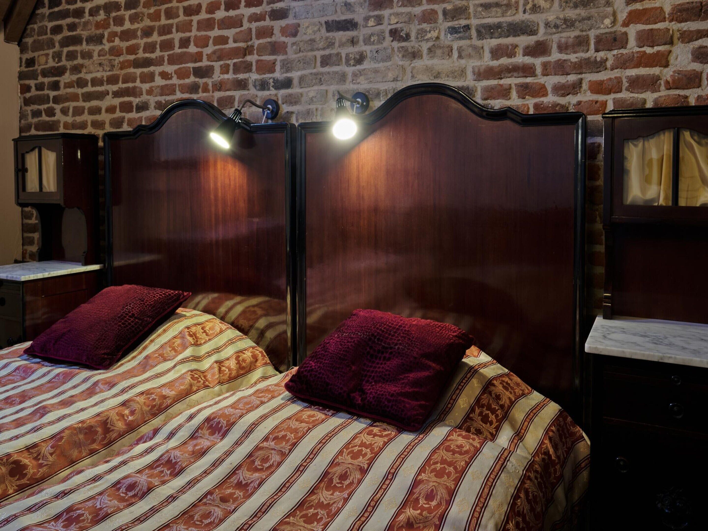 A room with a brick wall, a wooden headboard, two bedside tables, and a bed with striped bedding and two pillows.