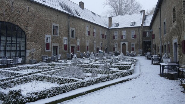 Een binnenplaats met besneeuwde heggen en buitenplaatsen.