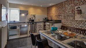 Een moderne keuken met roestvrijstalen apparatuur, een bakstenen muur en een glazen eettafel.