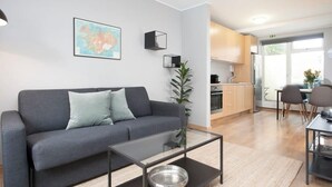 A modern living room with a grey sofa, a glass coffee table, and a kitchen in the background. - Tyr Downtown Studio Apartment (Reykjavík)