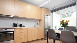 A modern kitchen with wooden cabinets, a stainless steel refrigerator, and a dining area with two chairs and a table. - Tyr Downtown Studio Apartment (Reykjavík)