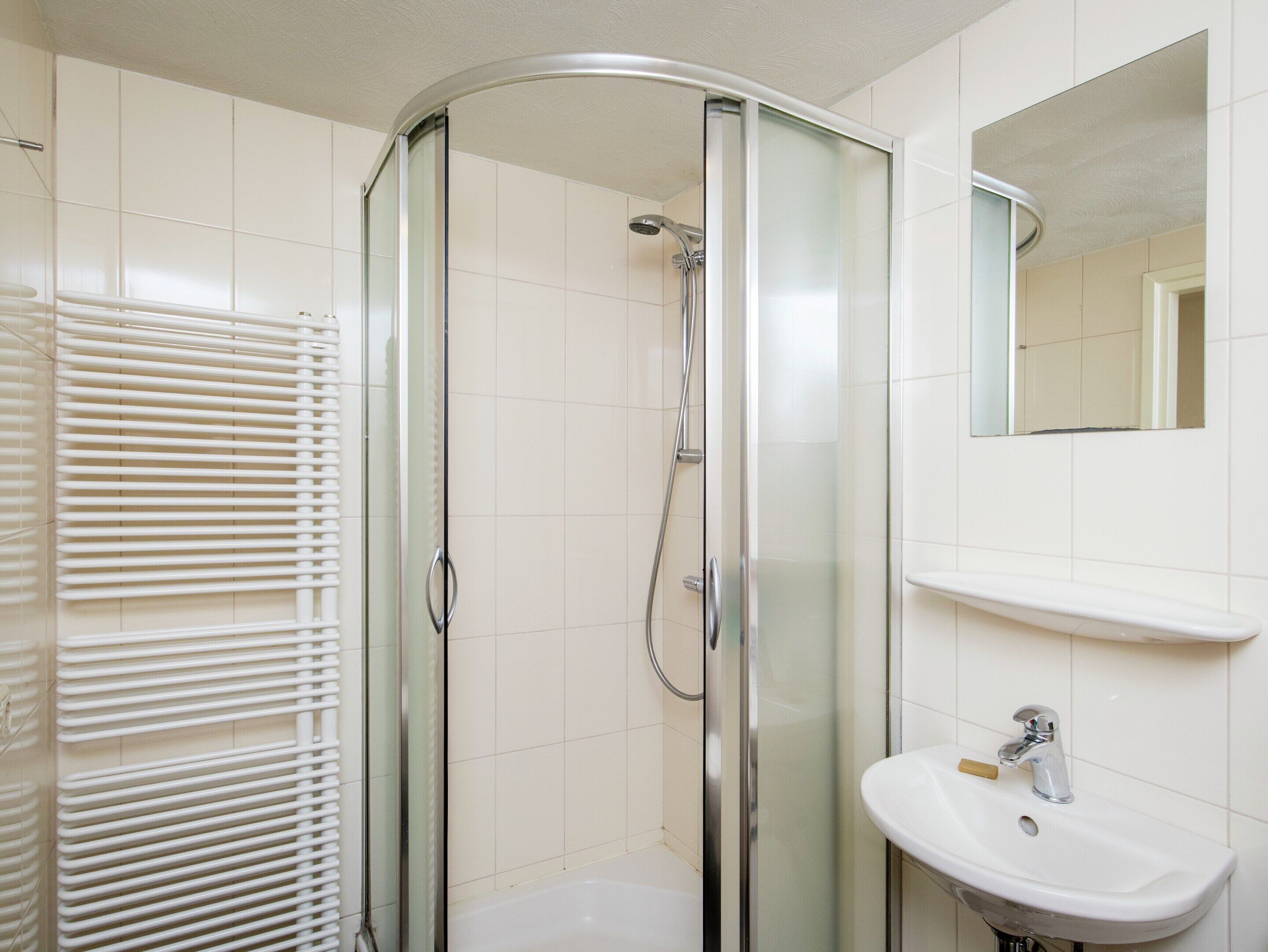 A bathroom with a glass-enclosed shower, a white sink, and a mirror above the sink.