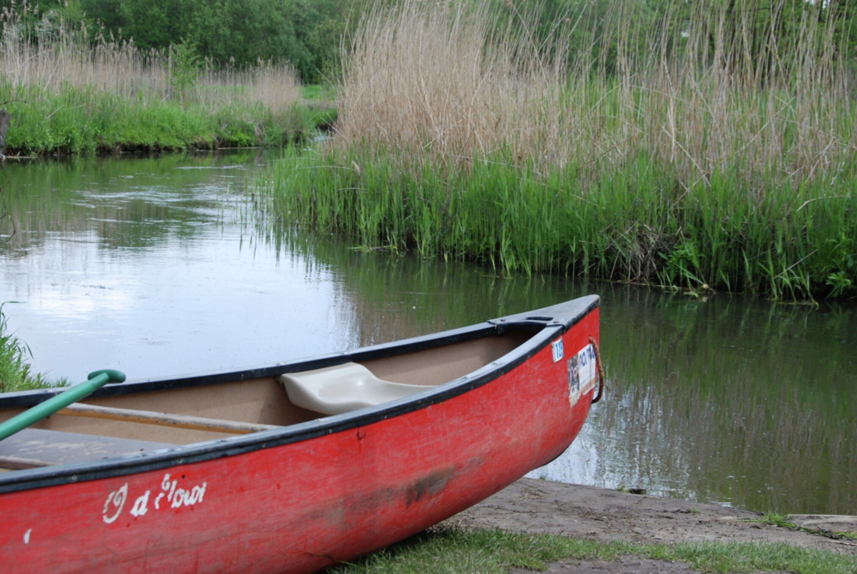 Un canoë rouge, avec une pagaie verte posée à côté, se trouve sur une rivière paisible.